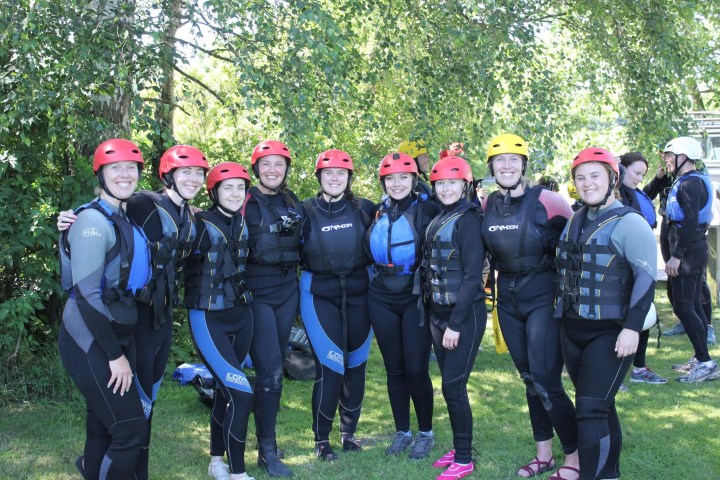 Group of people in wetsuits and helmets posing outdoors.