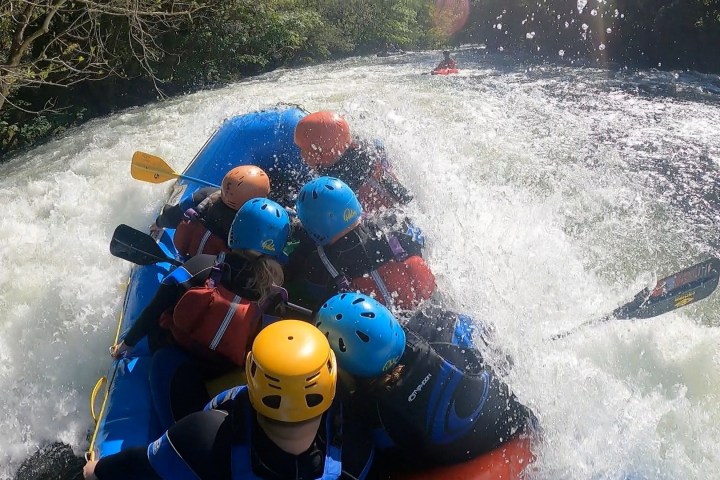 Group in helmets whitewater rafting through rough rapids.