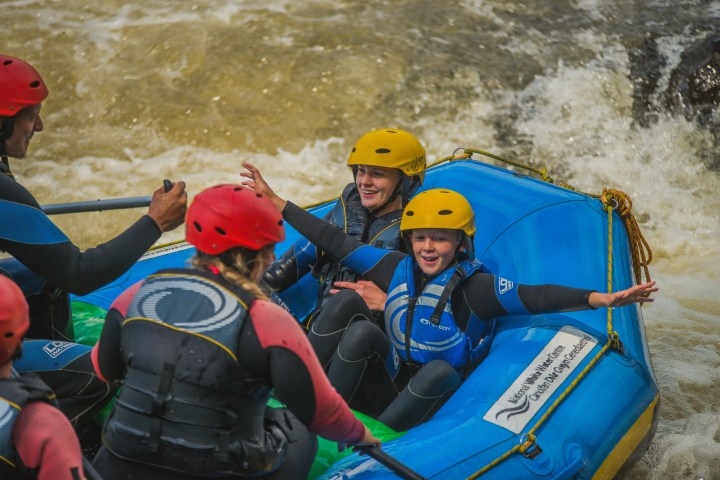 People in helmets rafting on a river with smiles and excitement.
